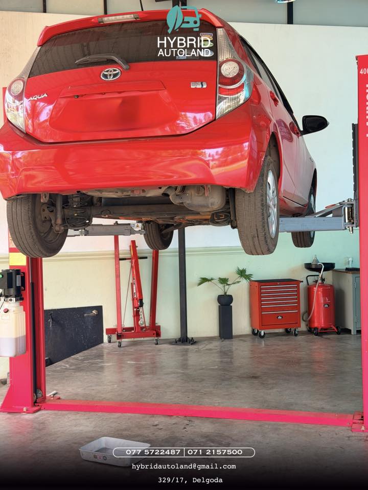 Red Toyota Aqua hybrid raised on a two-post lift