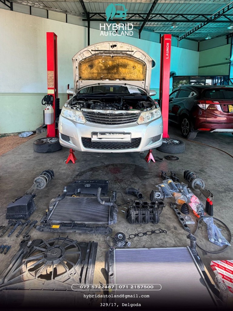 Silver Toyota sedan on jack stands with hood open and organized engine components laid out on the workshop floor